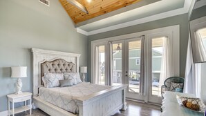 A bedroom with a large bed, a nightstand, a dresser, and a view of the outside through a sliding glass door. - Walk to Beach: Stunning Gulfport Getaway (Gulfport)