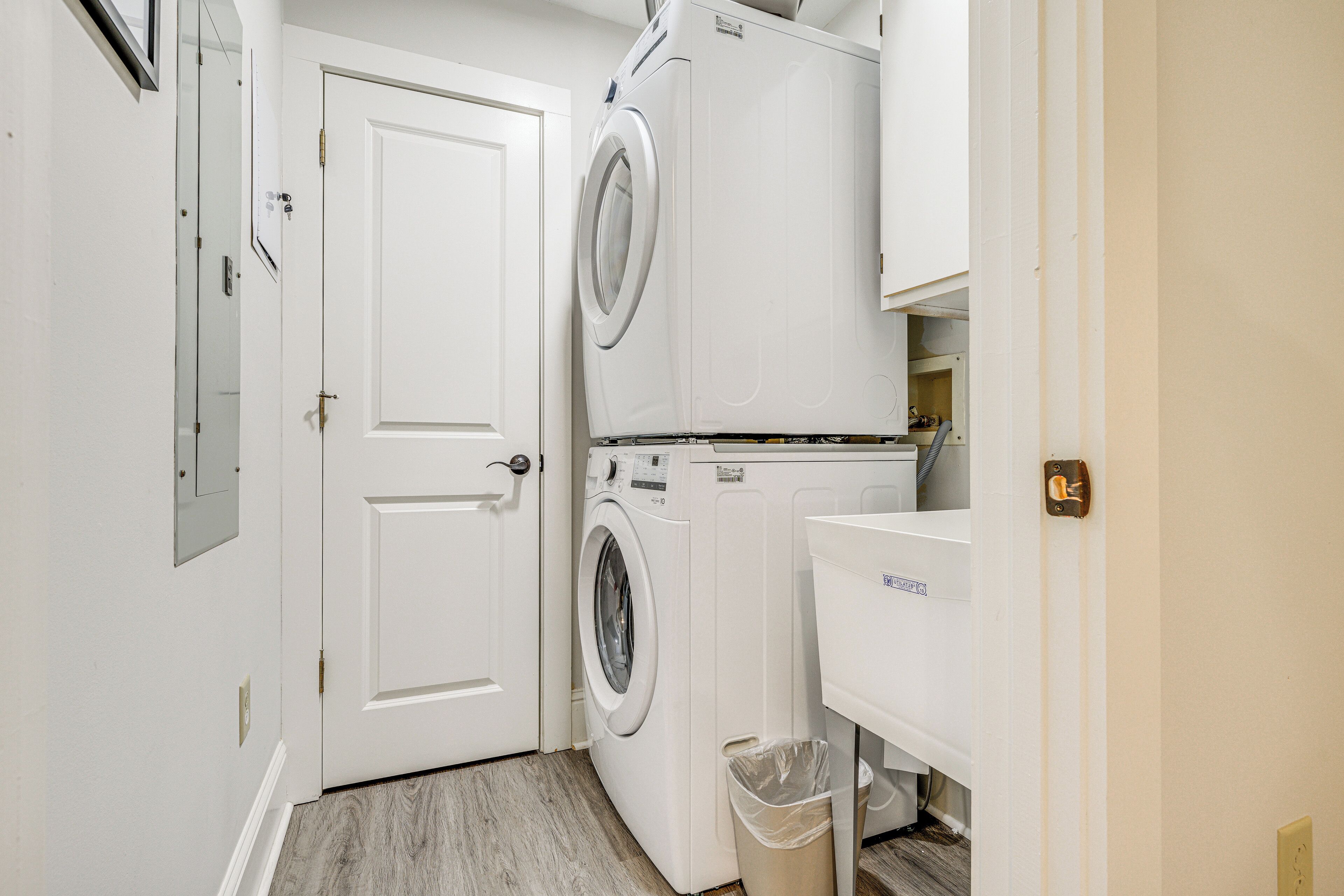 Une buanderie équipée d’un lave-linge et d’un sèche-linge à chargement frontal, d’une poubelle et d’un évier blanc.