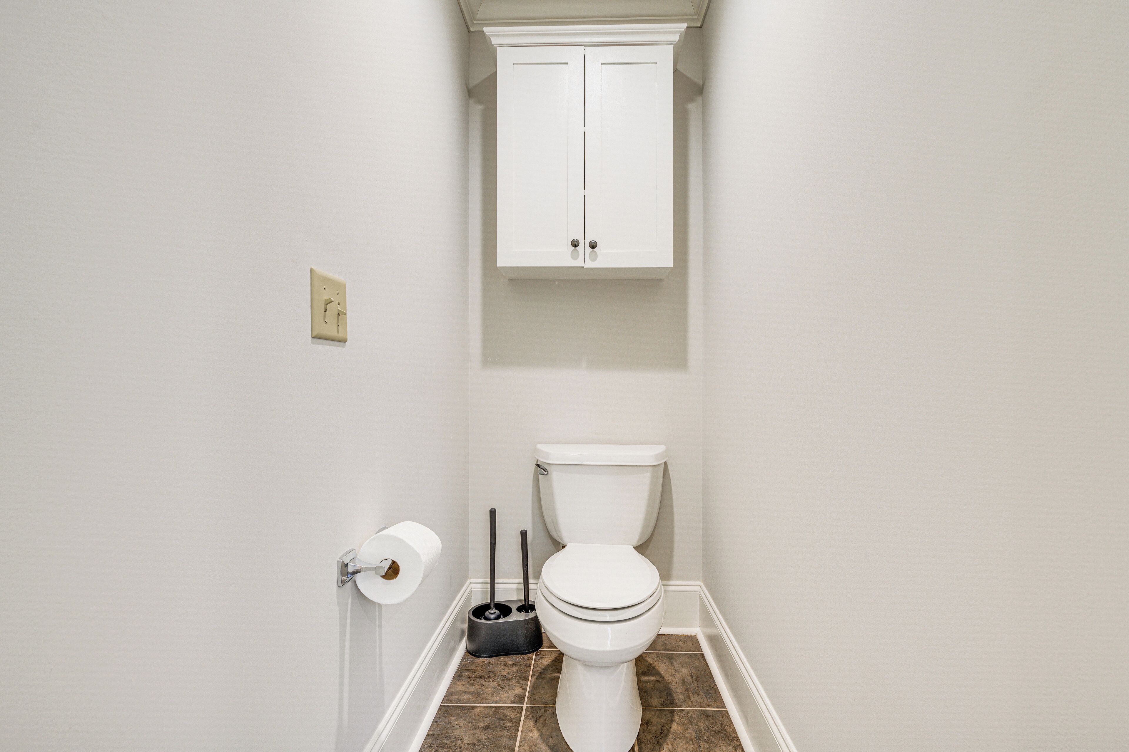 A bathroom with a toilet, a cabinet above it, and a toilet paper holder on the wall.