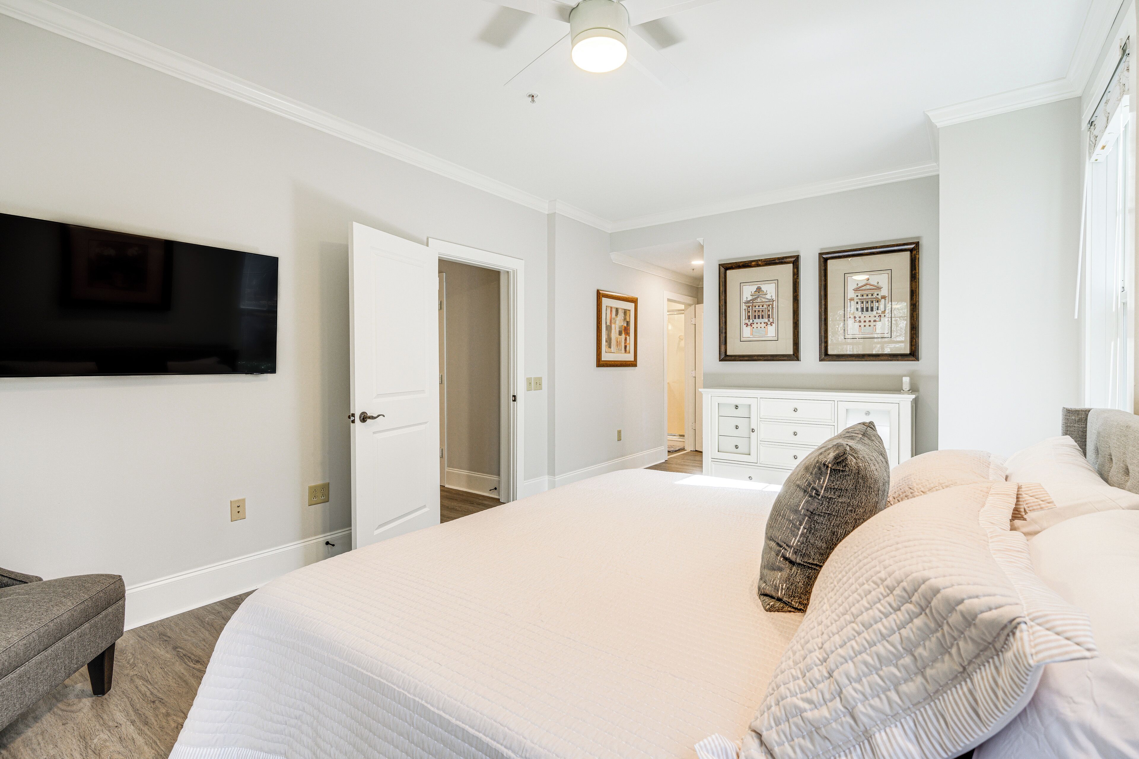 Quarto com cama grande, televisão de tela plana na parede, cômoda e porta para outro ambiente.