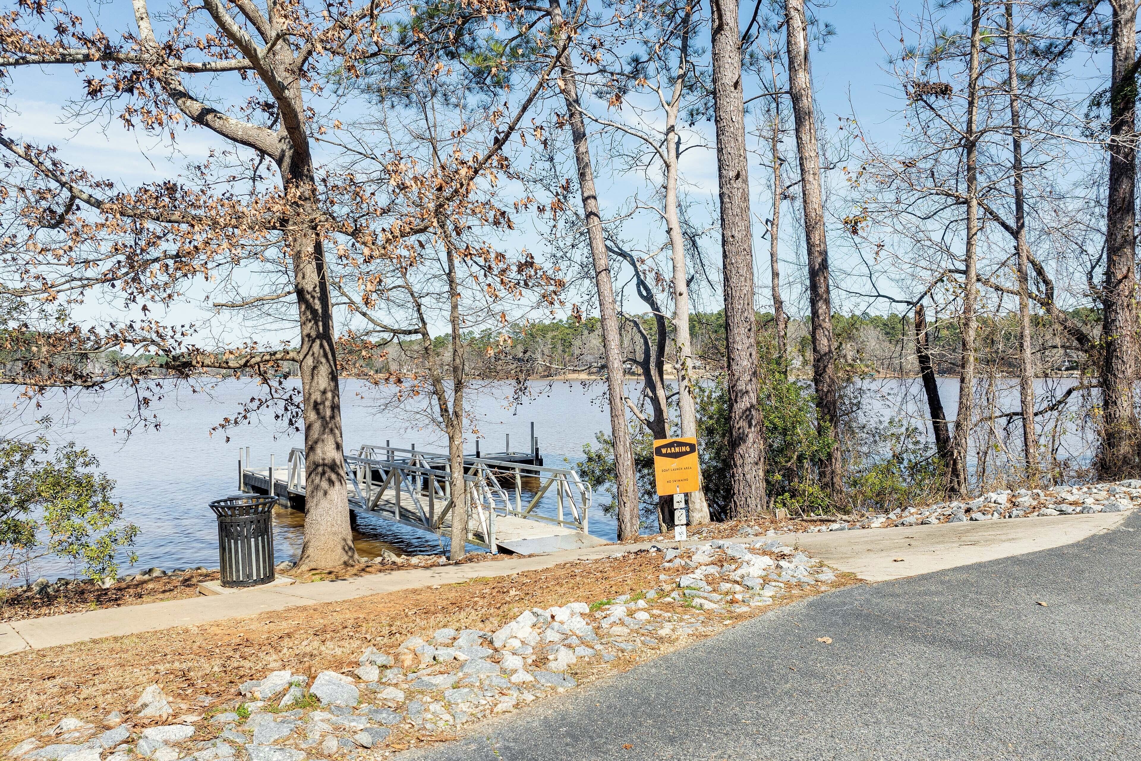 Una passeggiata lungo il lago con un molo di legno, un cartello di avvertimento giallo e un cestino.