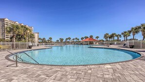 A large outdoor swimming pool with a tiled deck, surrounded by palm trees and a hotel building in the background. - Swim, Golf & Unwind: Barefoot Resort Condo (North Myrtle Beach)