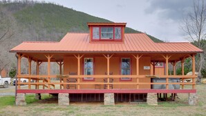 Une cabane en bois avec un toit rouge, des fondations en pierre et une véranda dotée de bancs.