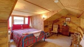 Une chambre mansardée chaleureuse, avec un lit, une commode, un fauteuil à bascule et un petit bureau.