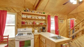 Une cuisine rustique aménagée dans une cabane en bois, avec une cuisinière à gaz, un évier et des étagères remplies de vaisselle.