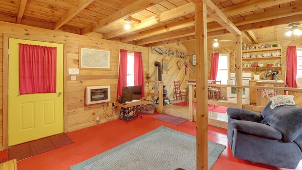 L’intérieur d’un chalet en bois, avec une porte jaune, des rideaux rouges, un téléviseur, une machine à coudre et un canapé.