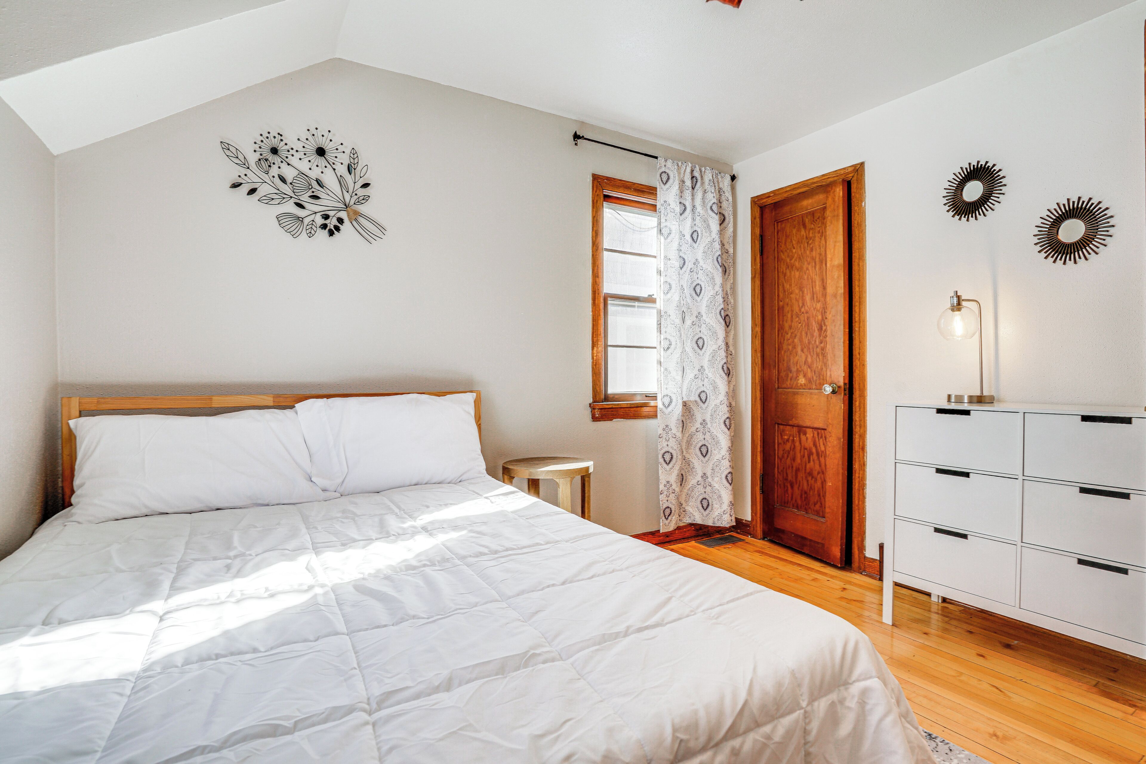 Un dormitorio con una cama, una puerta de madera, una mesita y un aparador.