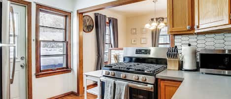 A kitchen with wooden cabinets, a stove, a microwave, and a window with curtains.