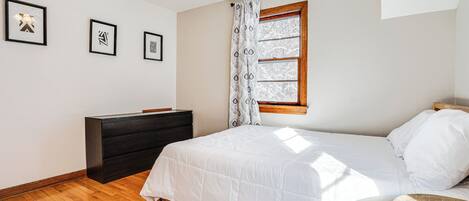 Un dormitorio con cama, cómoda, ventilador de techo y ventana con cortinas.