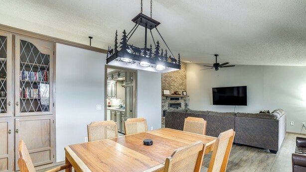 A dining area with a wooden table and chairs, a chandelier, a ceiling fan, and a TV mounted on the wall. - Spacious Holiday Island Escape w/ Deck & Gas Grill (Eureka Springs)