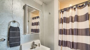 A bathroom with a white sink, a towel ring with a striped towel, a mirror, and a striped shower curtain.