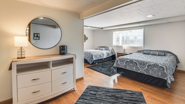 A bedroom with two beds, a dresser, a mirror, and a window.