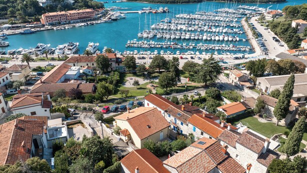 Una marina con numerosos barcos amarrados, rodeada de edificios residenciales con tejados de tejas rojas.