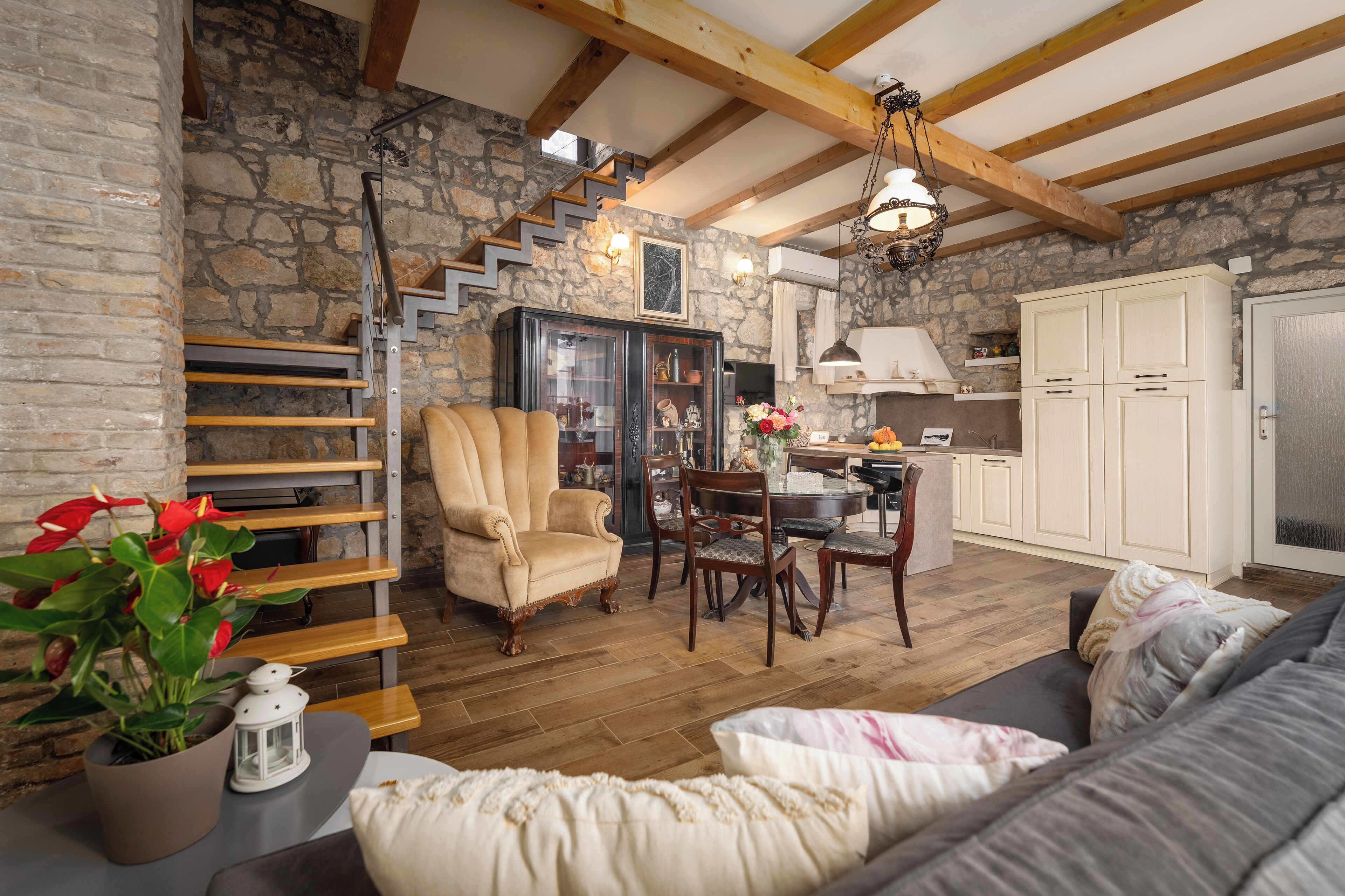 Un interior rústico con pared de piedra, vigas de madera, zona de comedor y un rincón de estar acogedor.