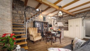 Un interior rústico con pared de piedra, vigas de madera, zona de comedor y un rincón de estar acogedor.
