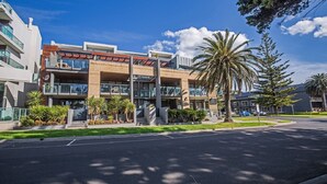 A modern multi-story building with a cafe on the ground floor, surrounded by palm trees and a clear sky. - Beachfront on the Esplanade (Cowes)