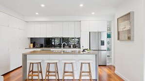A modern kitchen with white cabinetry, a central island with stools, a built-in oven, and a refrigerator. - Beachfront on the Esplanade (Cowes)