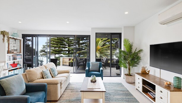 A modern living room with a sofa, coffee table, and TV. There is a balcony with a view of trees and a car. - Beachfront on the Esplanade (Cowes)