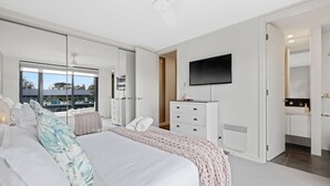 A modern bedroom with a large bed, a TV mounted on the wall, and a walk-in closet. - Beachfront on the Esplanade (Cowes)