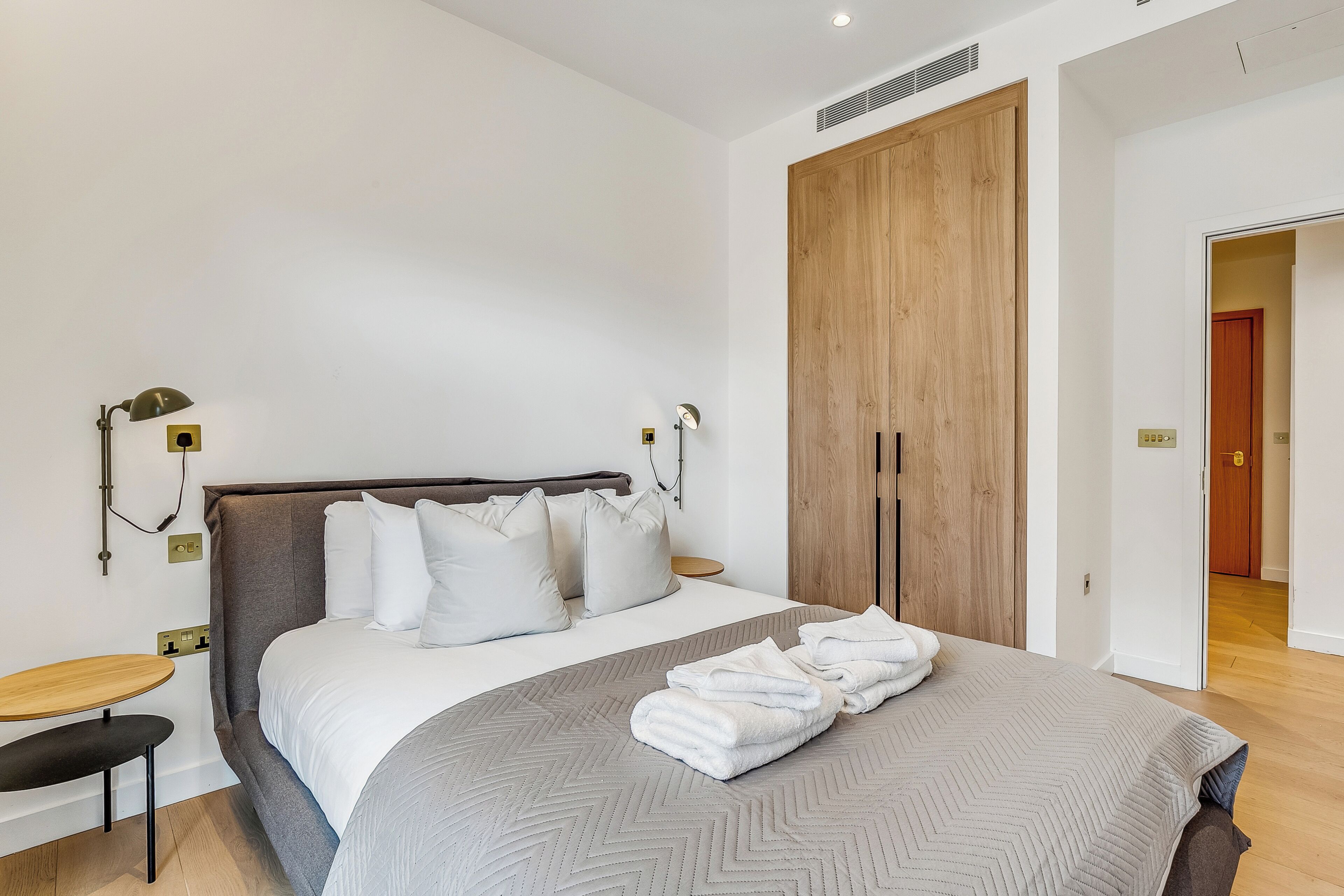 Een moderne hotelkamer met een groot bed, een houten garderobe, een nachtkastje en een wandlamp.