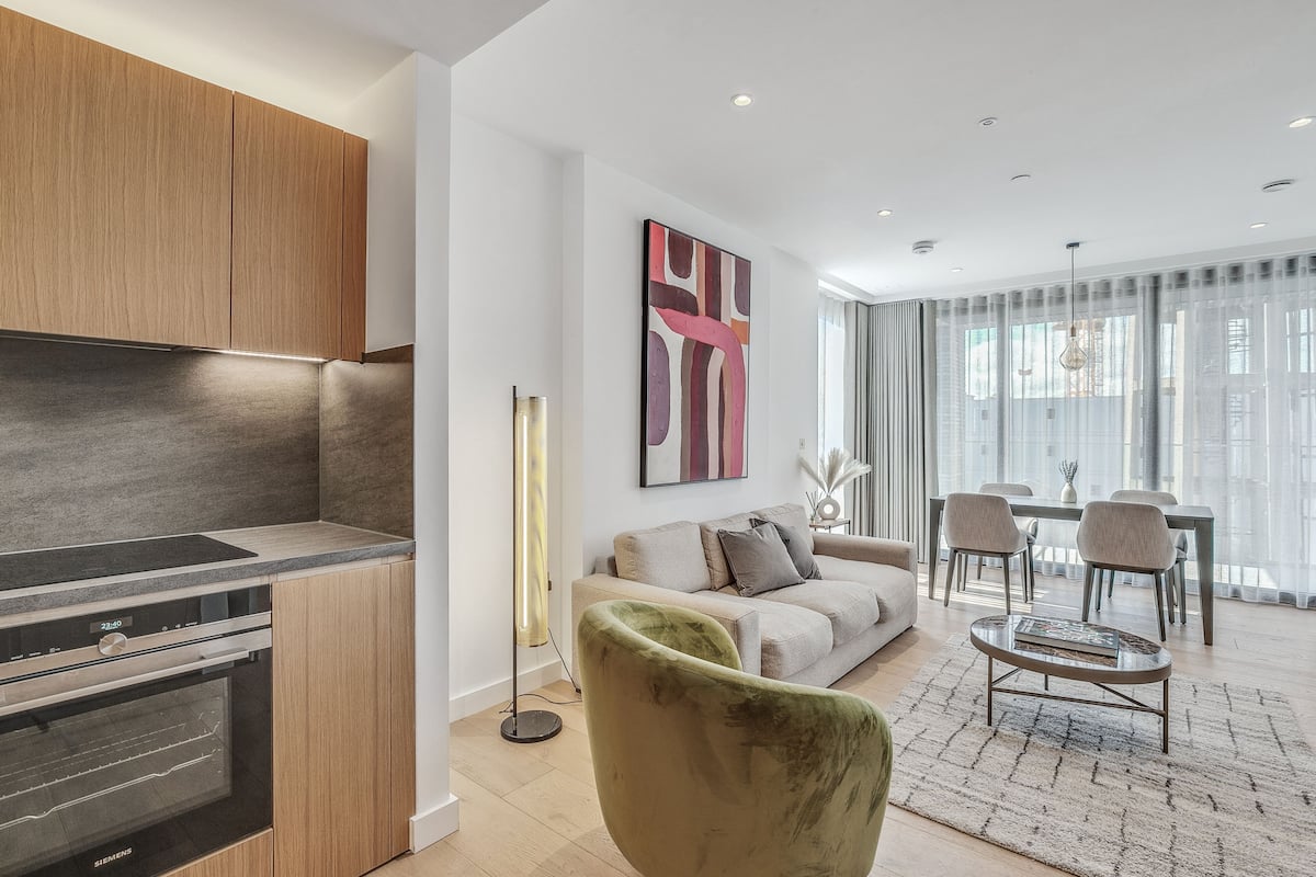 Una cocina moderna con electrodomésticos integrados, un comedor con mesa y sillas, y una sala de estar con sofá y un sillón verde.