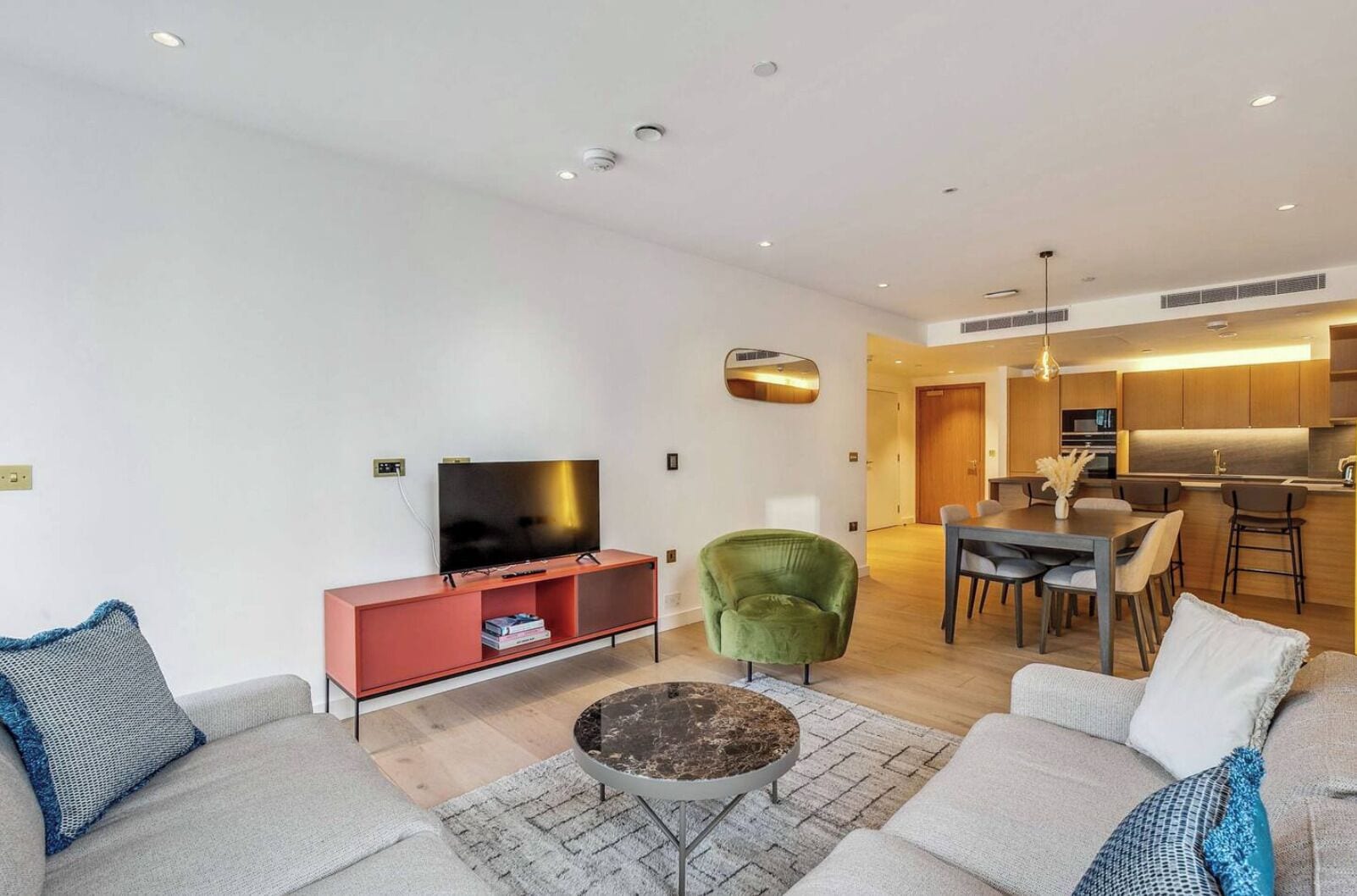 A modern living room with a flat-screen TV, a red entertainment unit, a green armchair, a coffee table, and a sofa with patterned cushions.