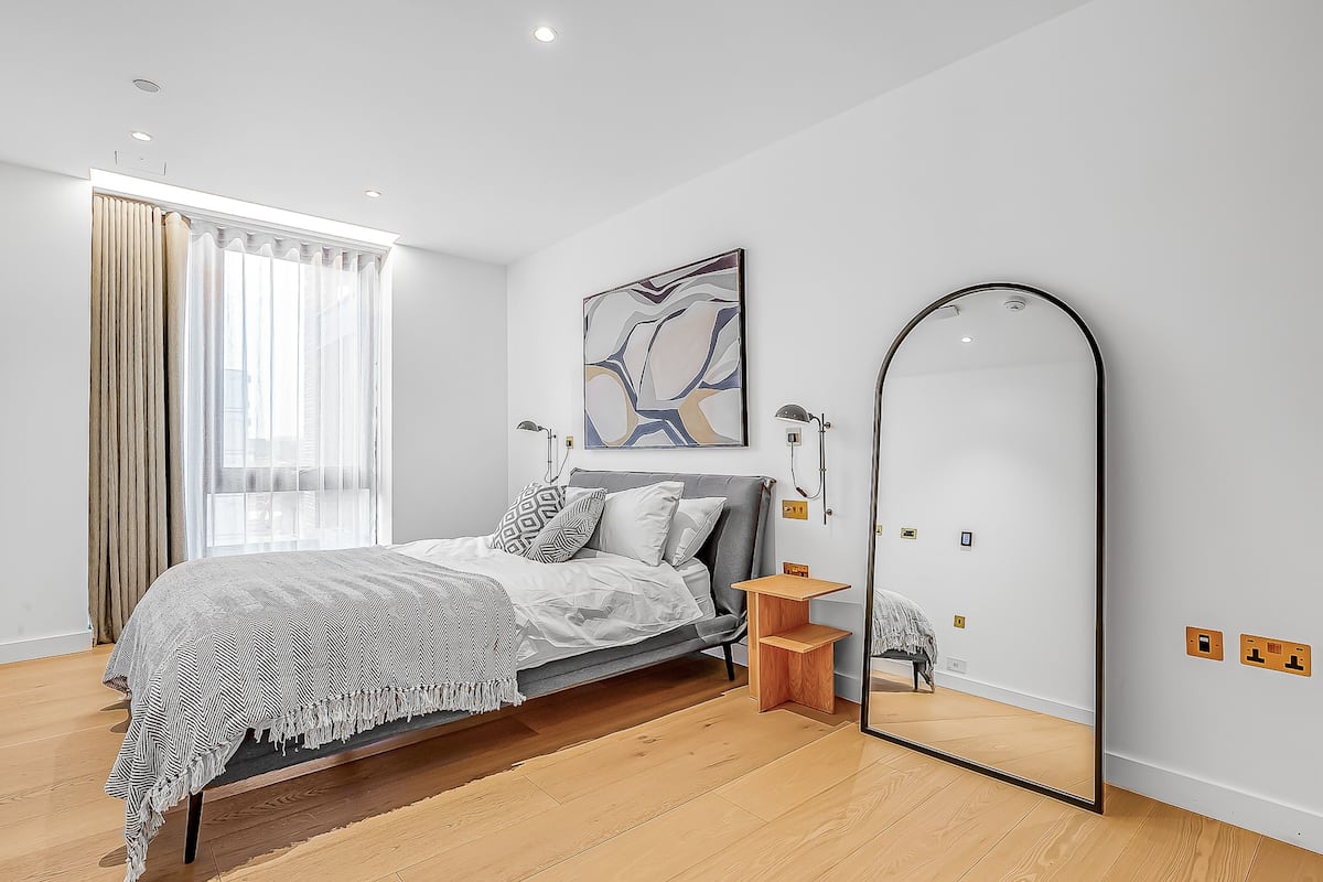 Un dormitorio moderno con cama, mesita de noche, espejo y una obra de arte.