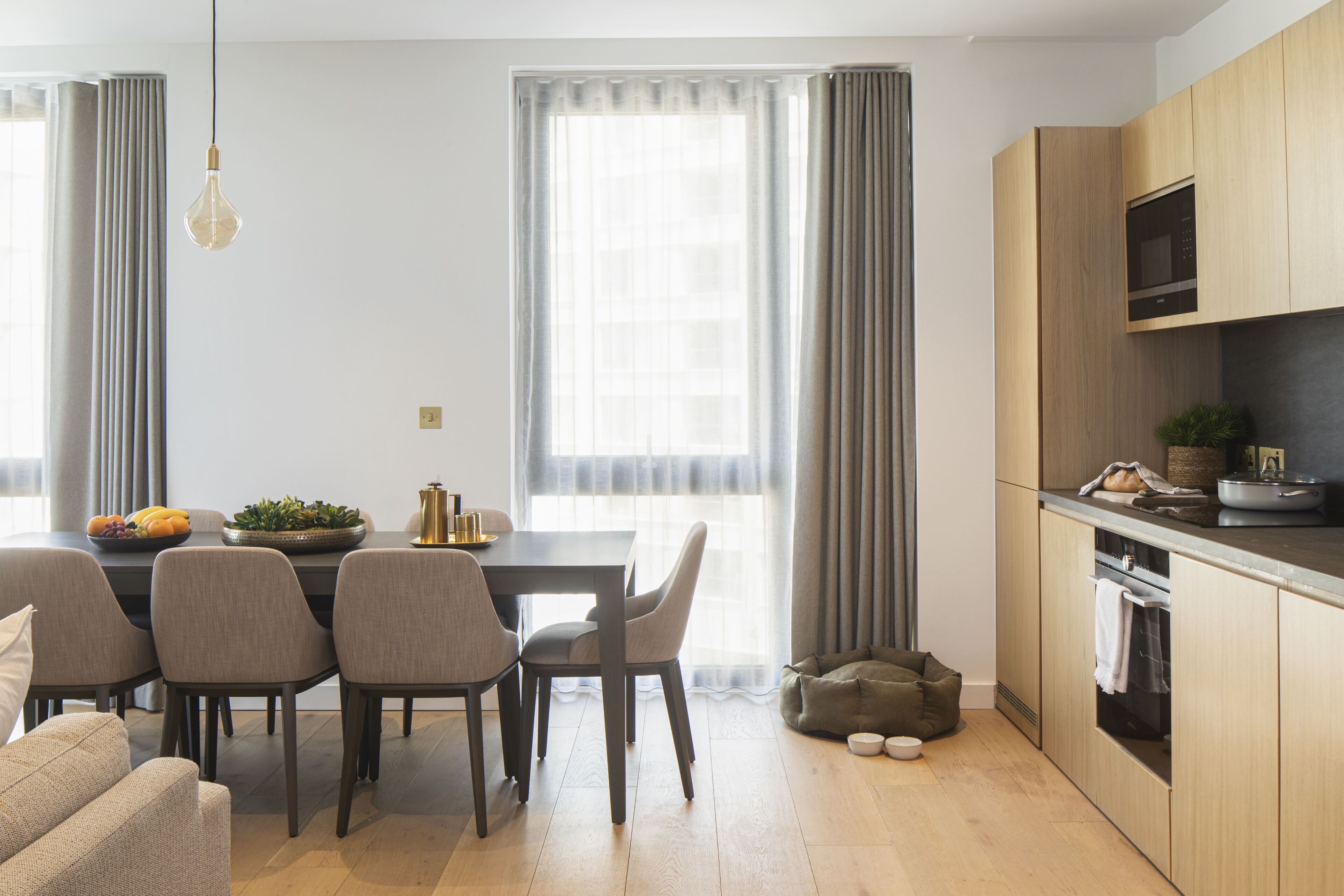 A modern kitchen with wooden cabinets, a built-in microwave, and a dining area with a table and chairs.