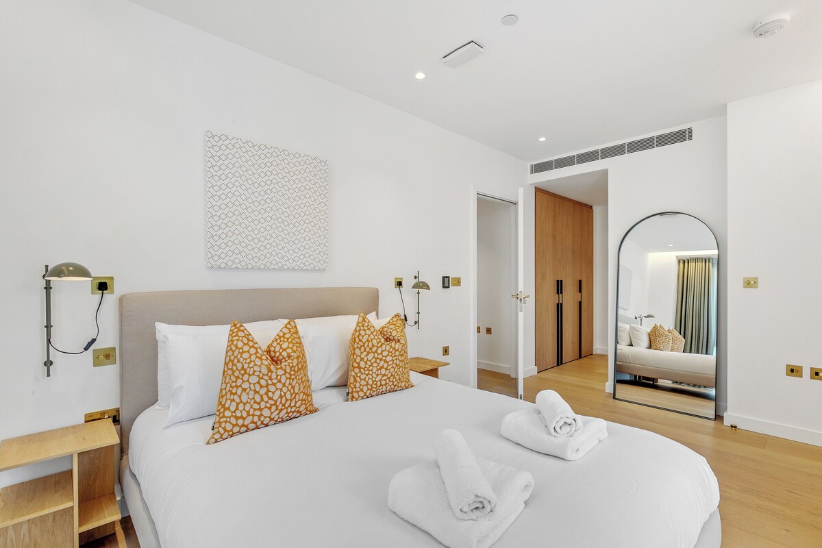 A modern hotel room with a large bed, a bedside table, a wall-mounted lamp, and a mirror.