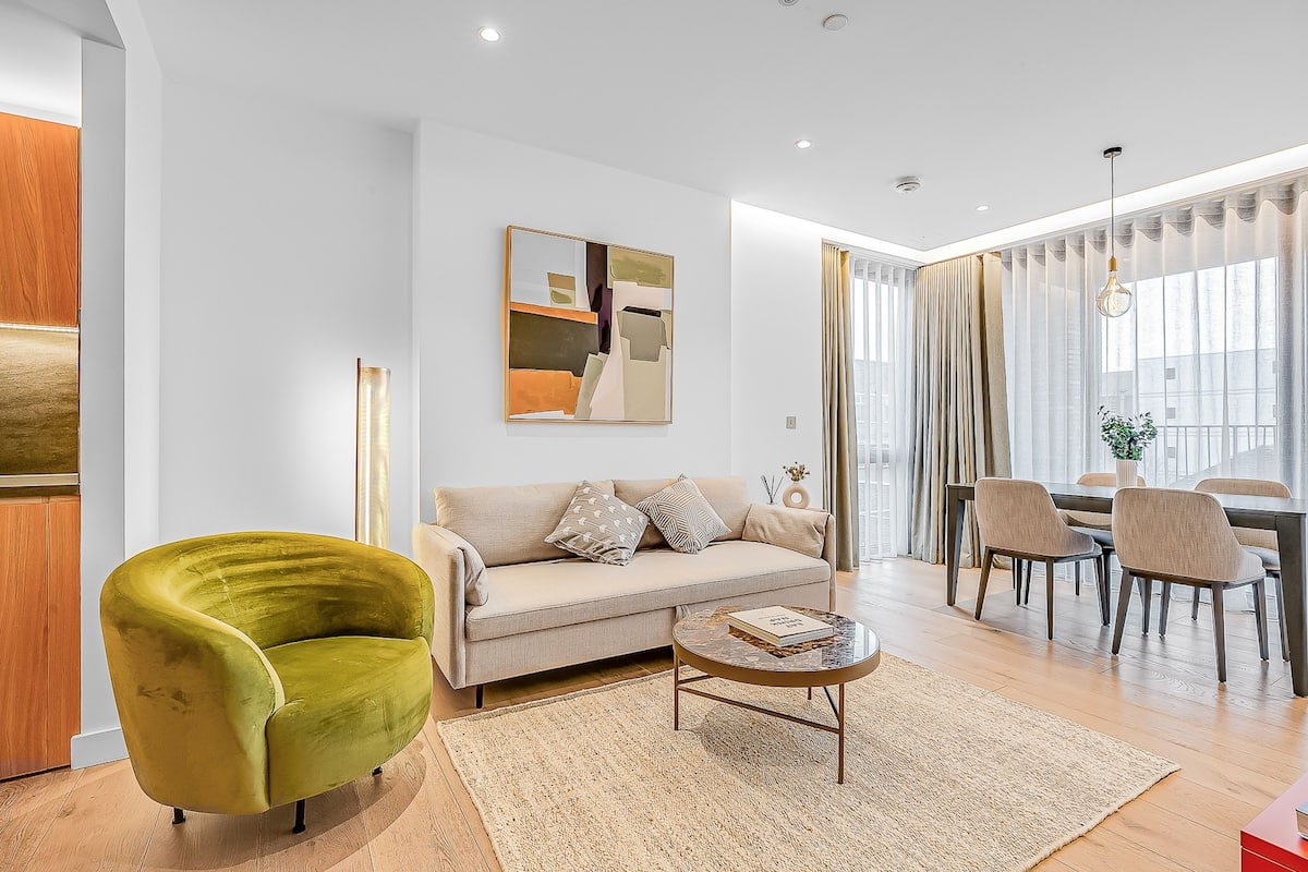 Una sala de estar moderna con un sofá, un sillón verde, una mesa de centro y una zona de comedor con sillas y una mesa.