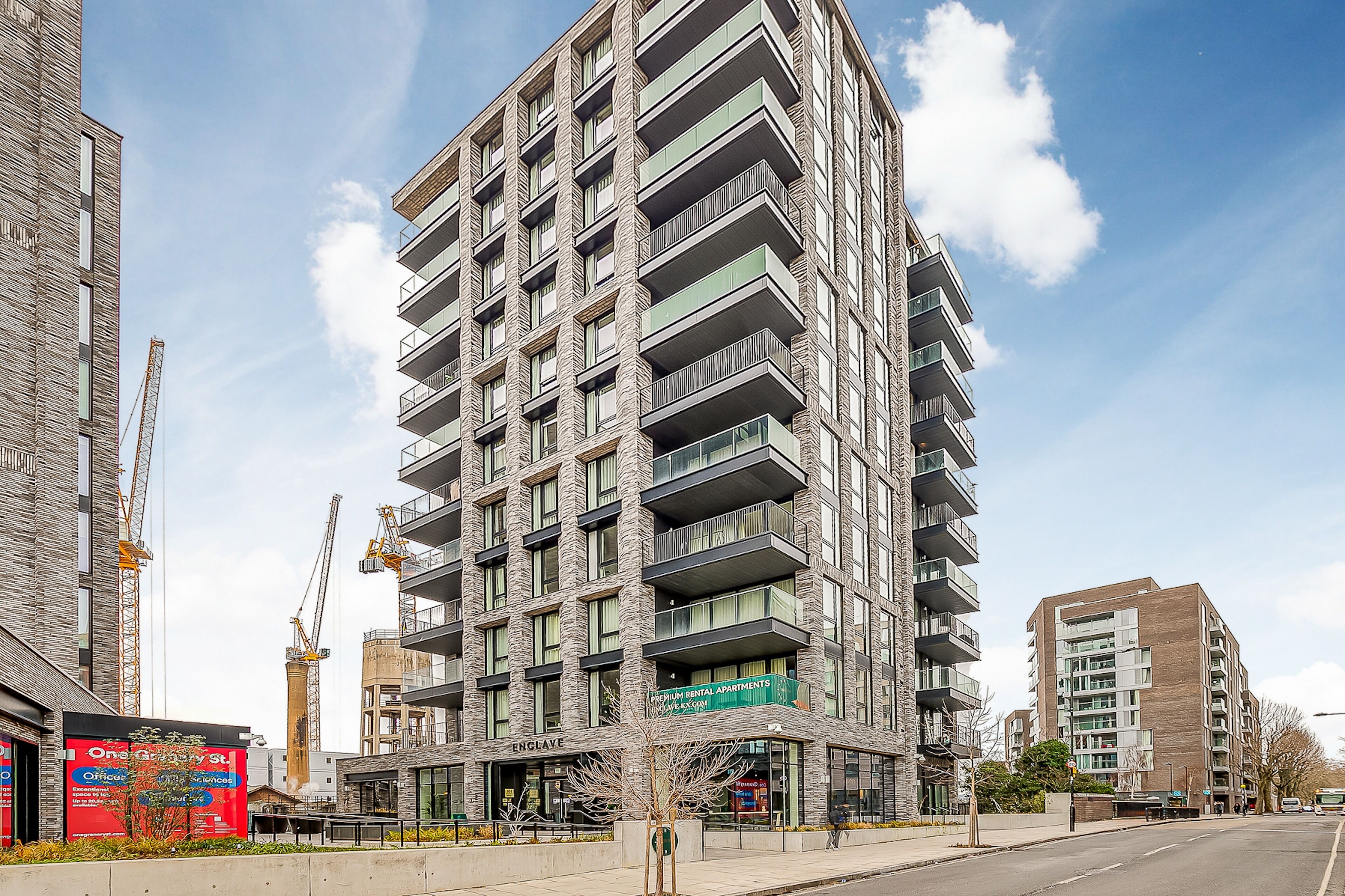 Un edificio de varios pisos con balcones, una grúa de construcción y un cartel que anuncia apartamentos de alquiler de primera calidad.