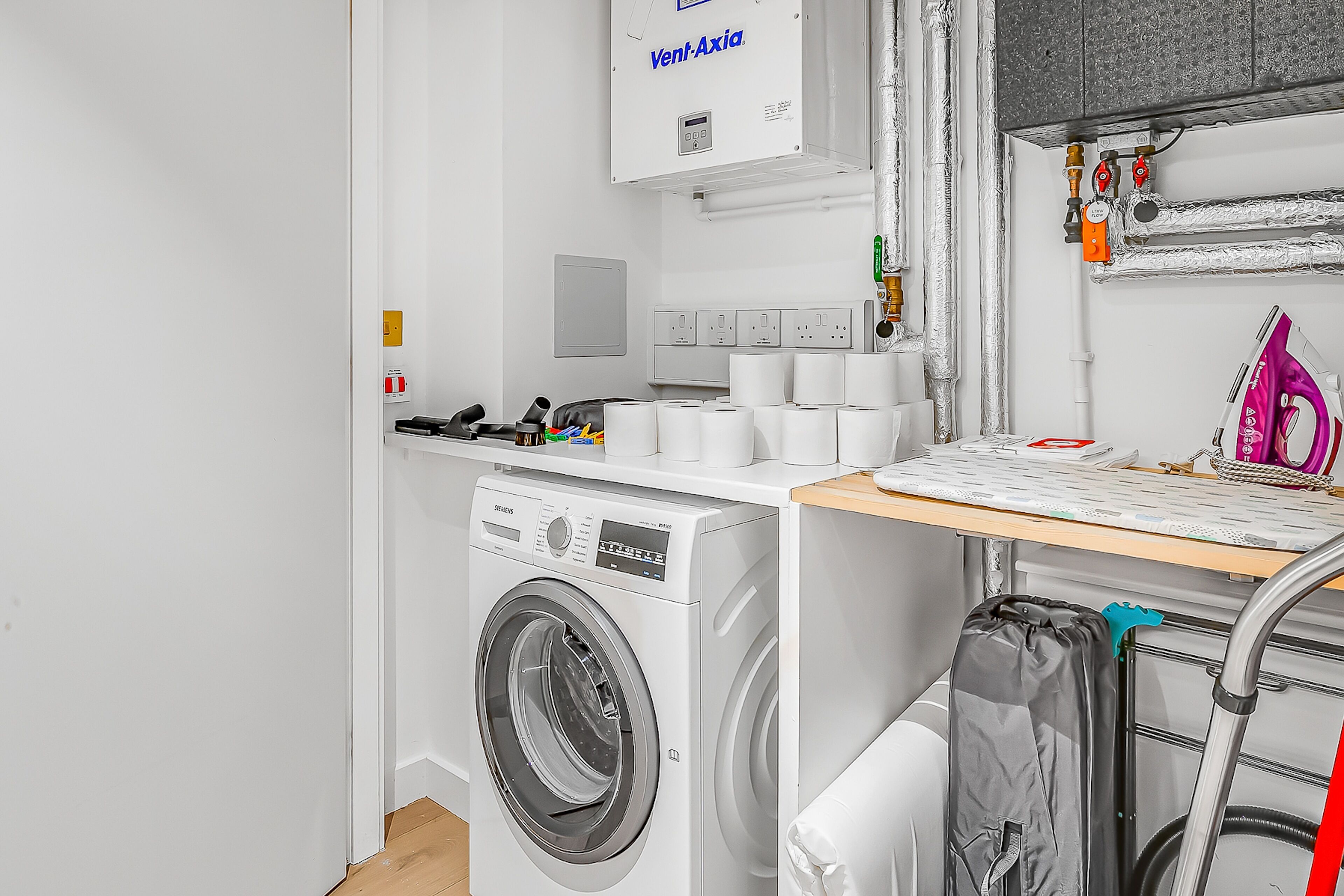 Een wasruimte met een wasmachine, een droogrek en een strijkplek.