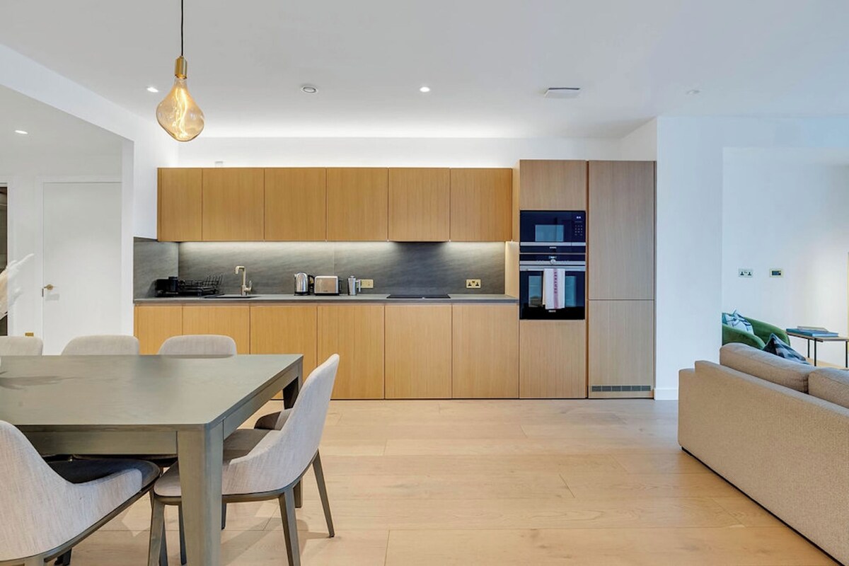 A modern kitchen with wooden cabinets, a built-in oven, and a dining area with a table and chairs.