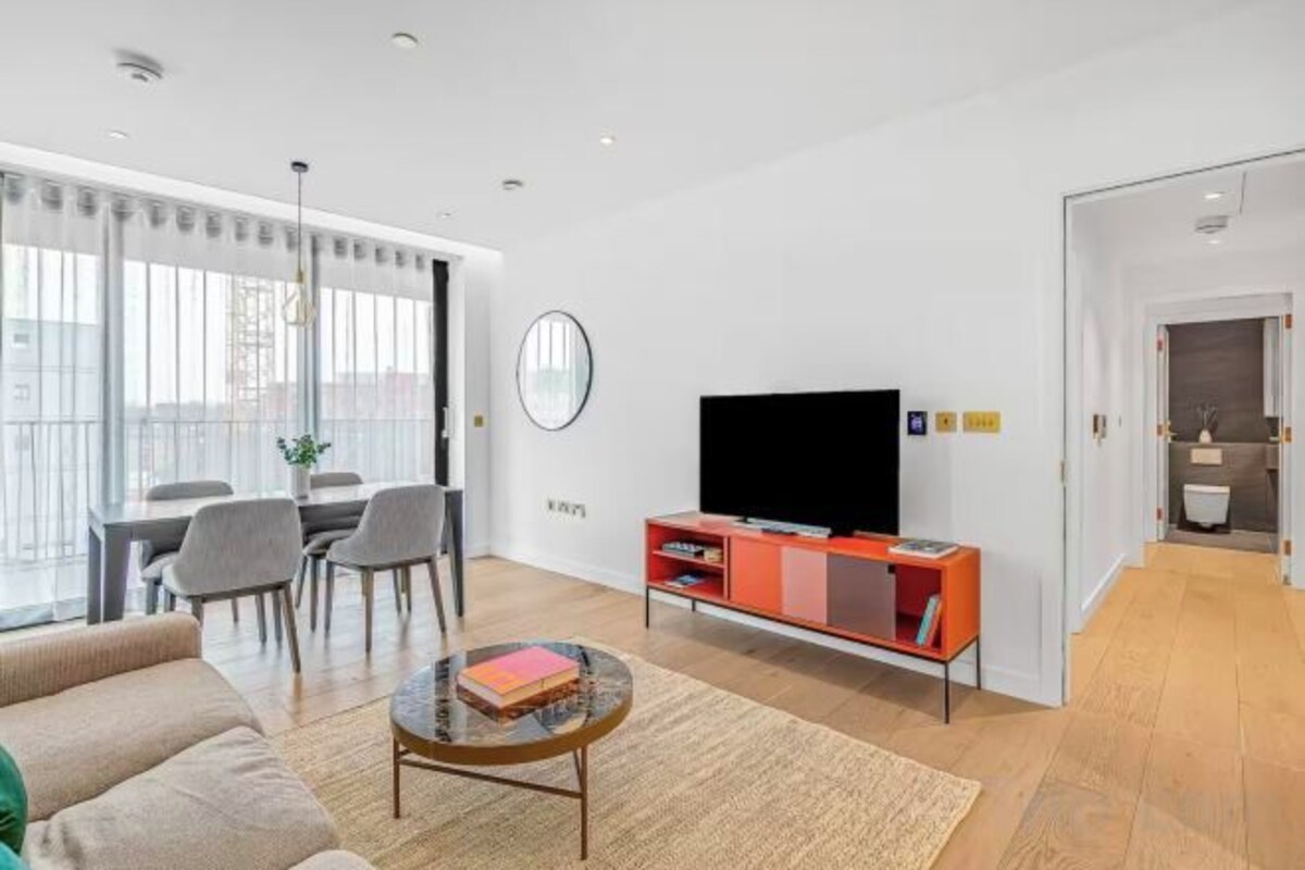 A modern living room with a sofa, a coffee table, a TV on a stand, and a dining area with chairs and a table.