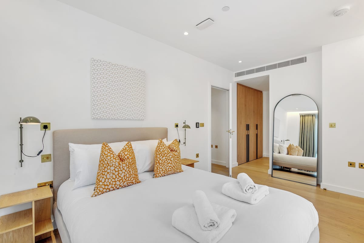 A modern hotel room with a large bed, a bedside table, a wall-mounted lamp, and a mirror.