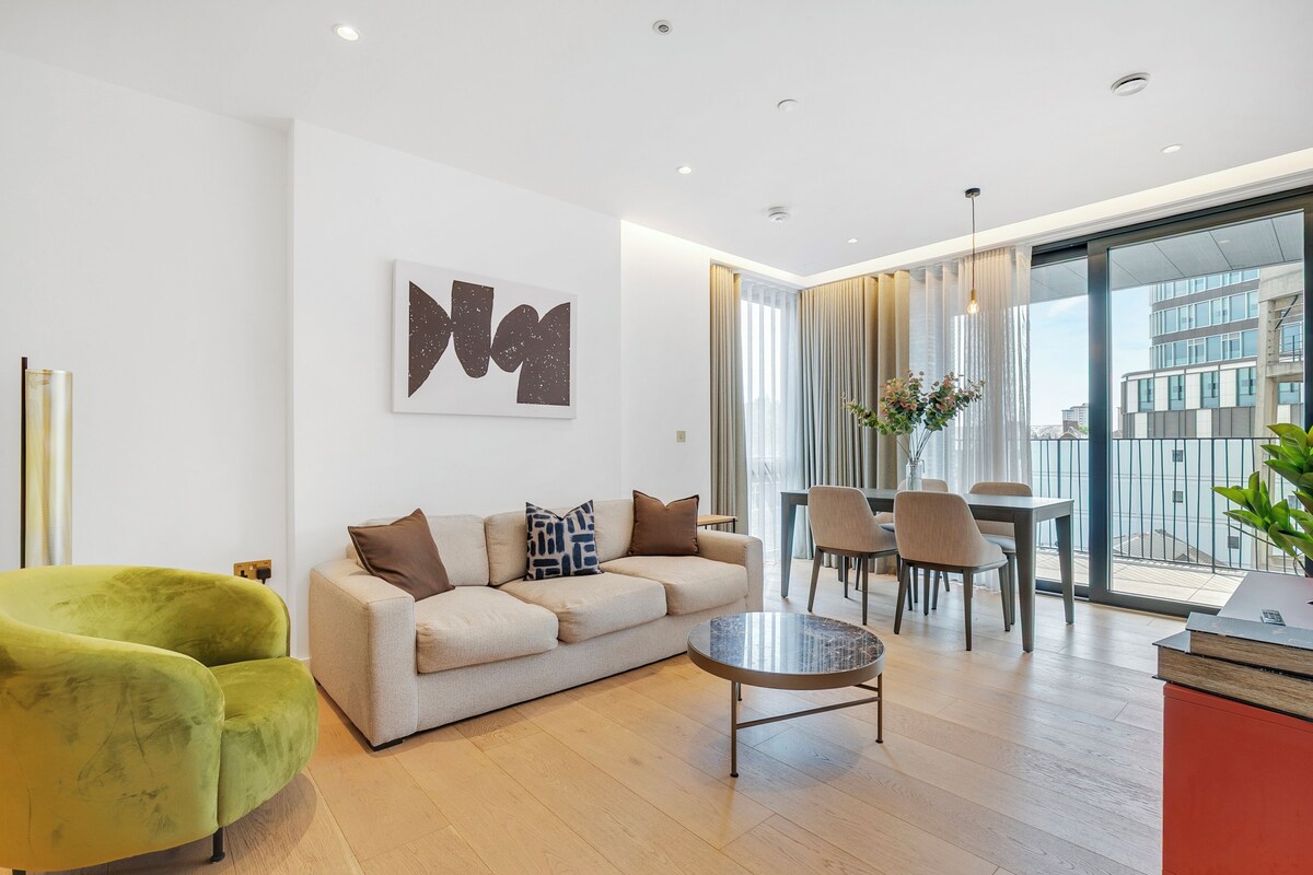 A modern living room with a sofa, a green armchair, a coffee table, and a dining area with chairs and a table.