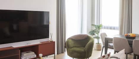 A modern living room with a flat-screen TV, a green armchair, a sofa, and a dining area with a table and chairs.
