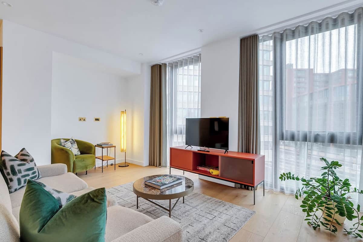 Una sala de estar moderna con un sofá, una mesa de centro, un televisor sobre un mueble bajo y una planta.