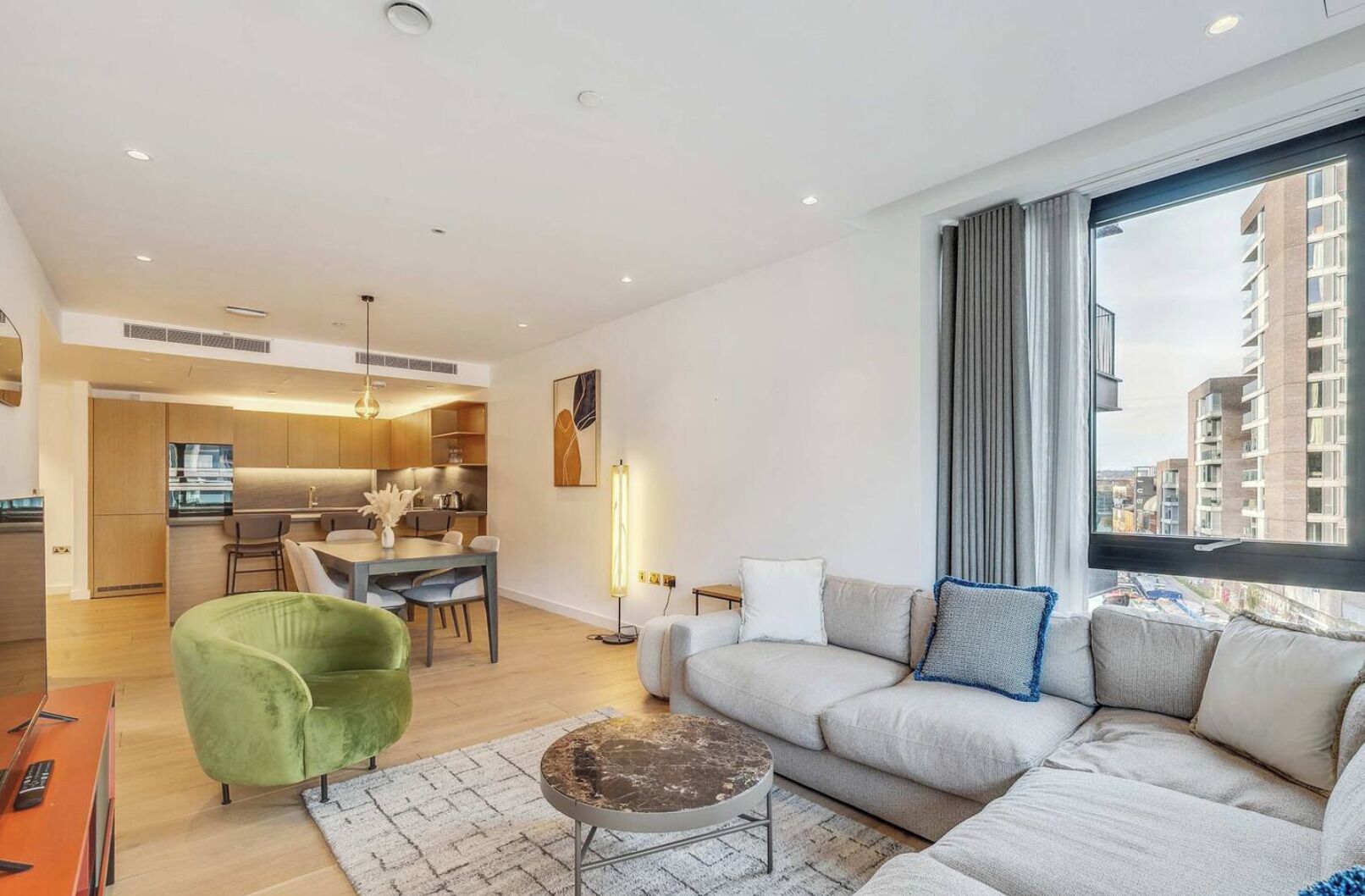 A modern apartment with a dining area, kitchen, and living room with a large window.