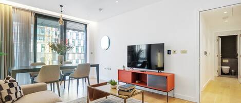 A modern living room with a sofa, coffee table, TV, and dining area.