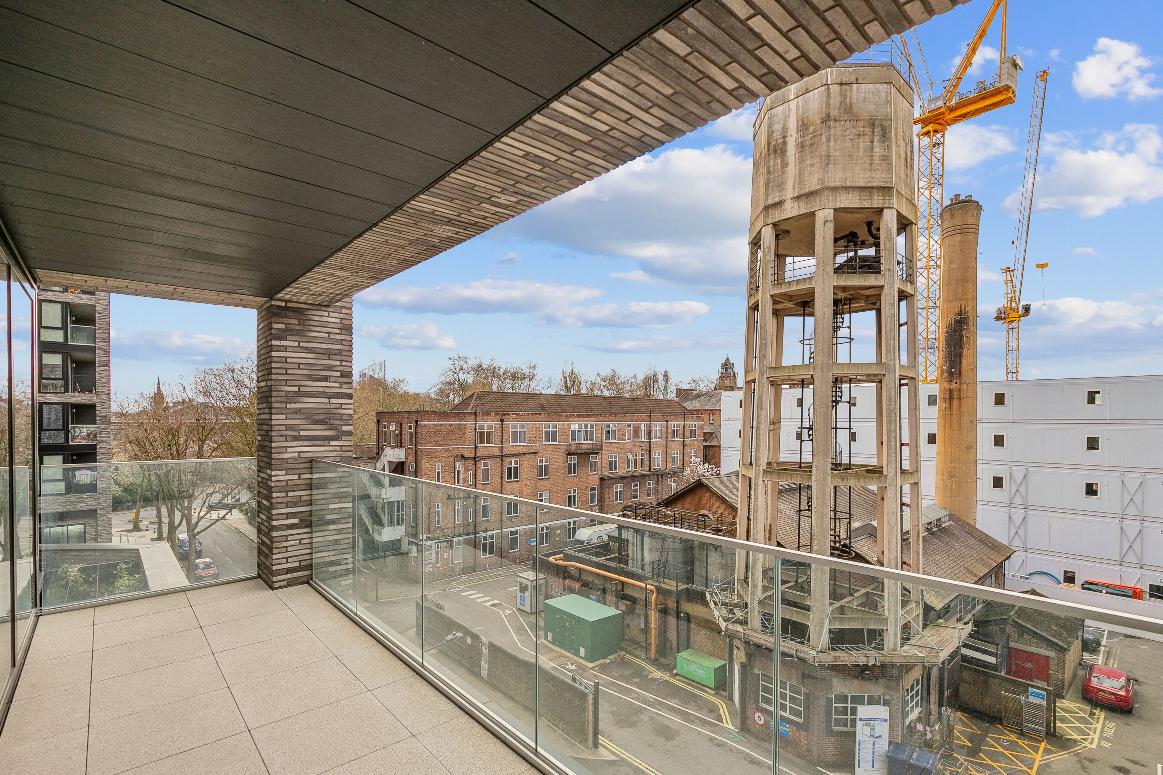 Un bâtiment moderne doté d’un balcon en verre donnant sur un chantier de construction et des immeubles résidentiels.