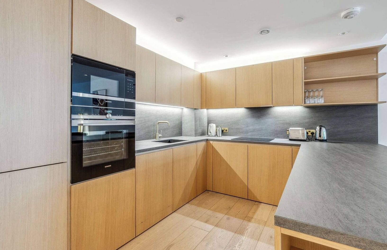 Eine moderne Küche mit Holzausstattung, einem eingebauten Backofen und einer Arbeitsplatte mit Wasserkocher.