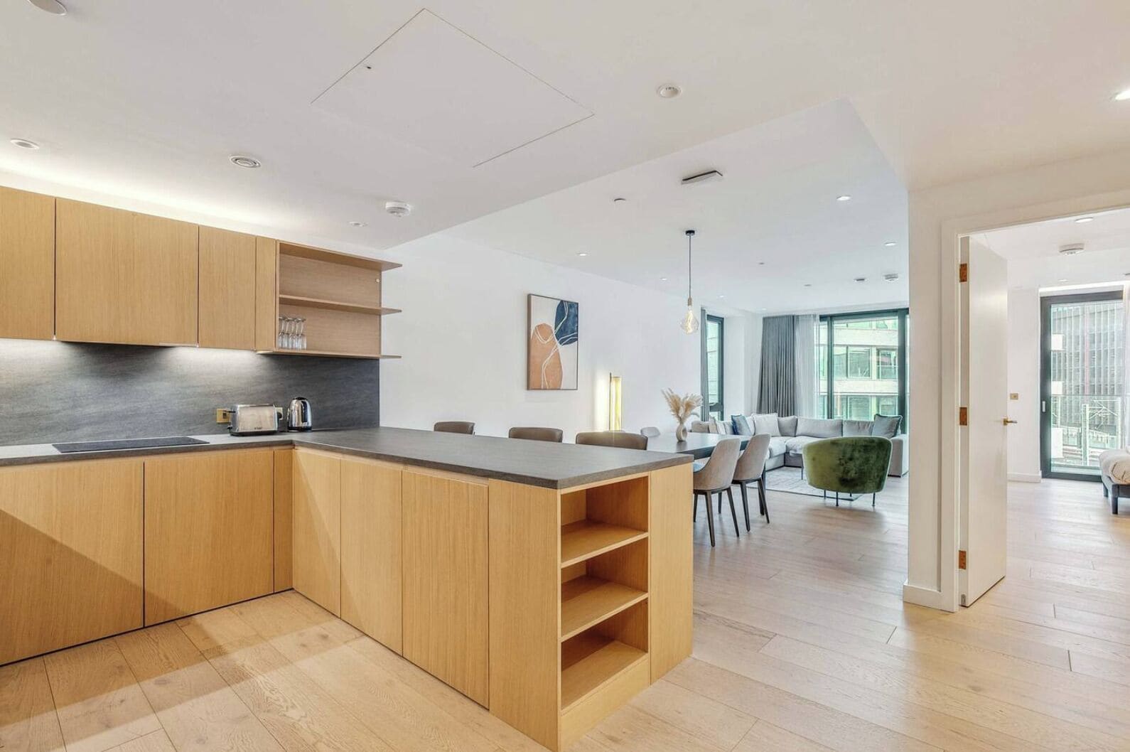 Eine moderne Küche mit Holzschnitzschränken und einer zentralen Kochinsel, die in einen Essbereich mit einem grünen Sofa und Blick auf die Stadt übergeht.