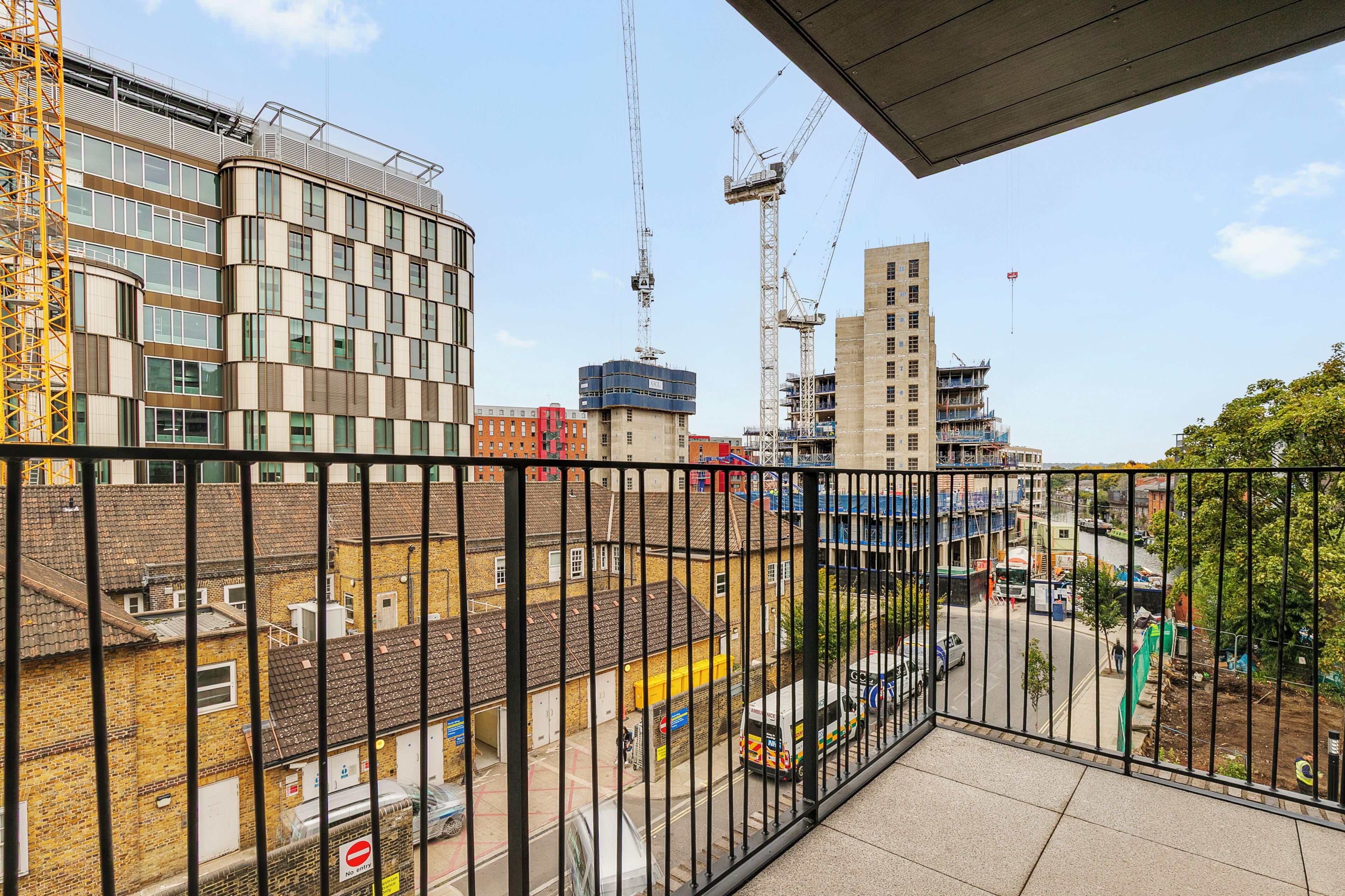 Un balcon offrant une vue sur un chantier de construction, une rivière et un mélange de bâtiments modernes et anciens.