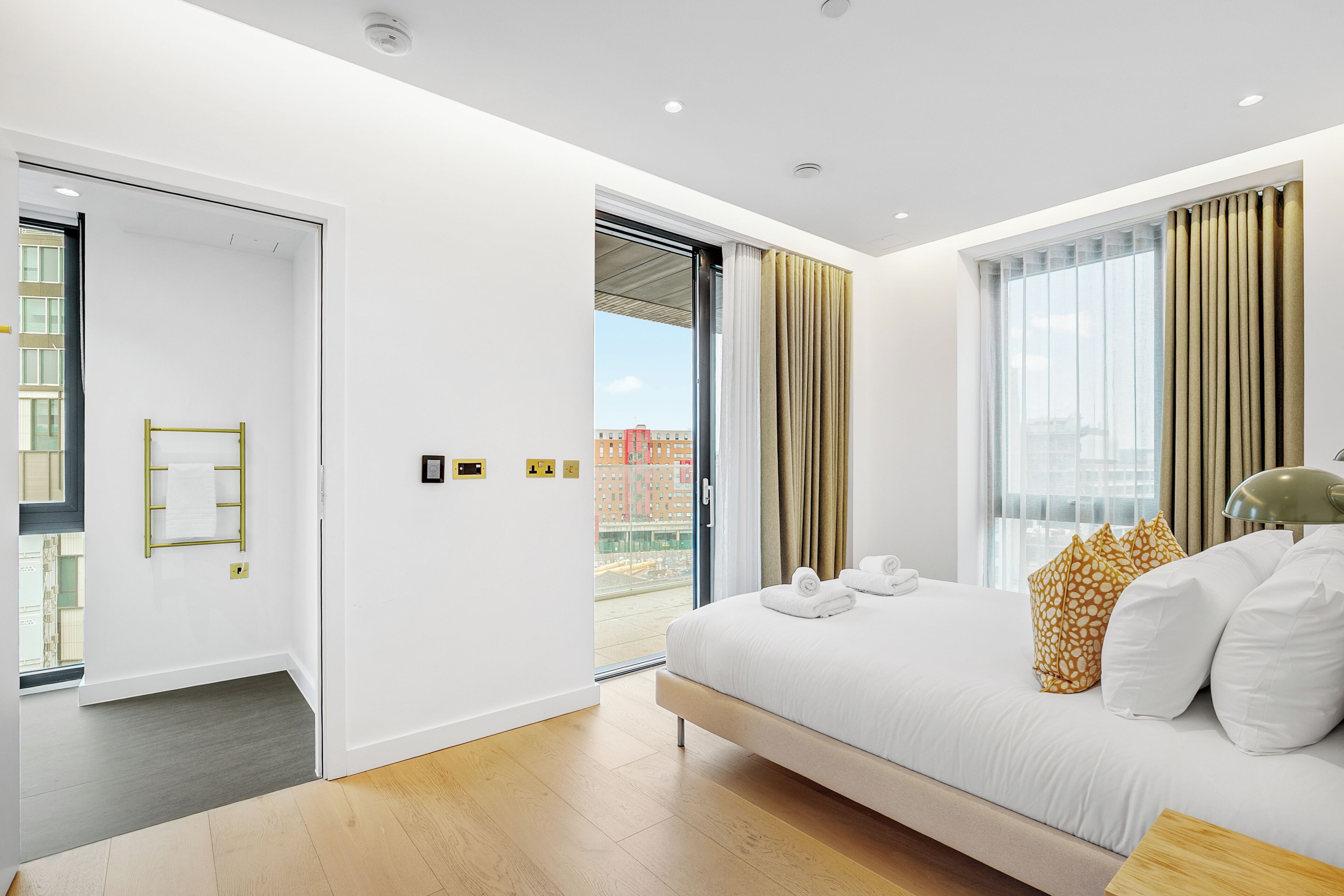 A modern hotel room with a large bed, a sliding glass door to the balcony, and a view of the cityscape.
