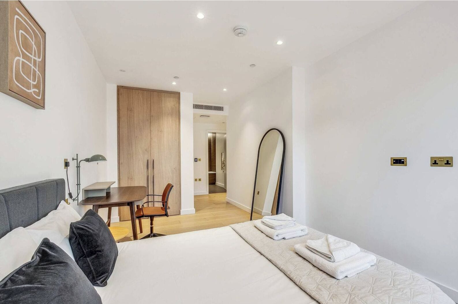Une chambre d’hôtel moderne équipée d’un lit, d’un bureau, d’une chaise et d’un grand miroir.