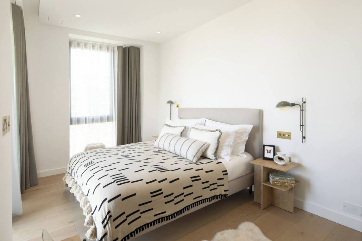 Un dormitorio moderno con una cama grande, una mesita de noche y un pequeño mueble auxiliar.