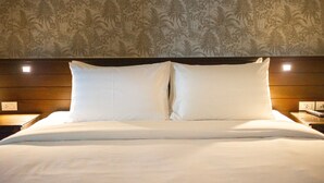 Een netjes opgemaakt bed met witte lakens en twee kussens, een houten hoofdbord en een muur met een tropisch palmboompatroon.