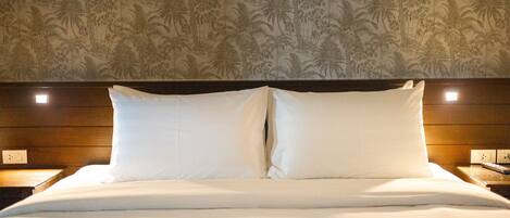 A neatly made bed with white linens and two pillows, a wooden headboard, and a wall with a tropical palm tree pattern.