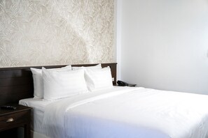 A neatly made bed with white linens and pillows, a wooden headboard, and a nightstand with a phone and remote control. - Singharaj Boutique Hotel (Chiang Mai)